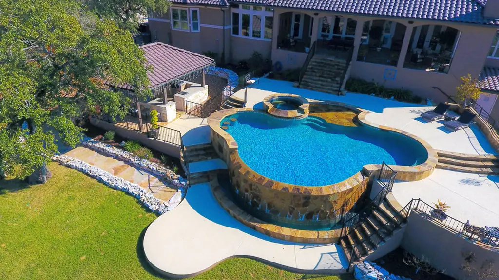 Aerial view of a freeform gunite pool and raised spa set on a stone wall above a lawn