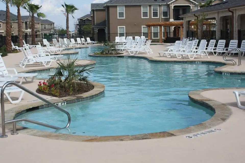Large freeform community pool at an apartment complex lined with white loungers