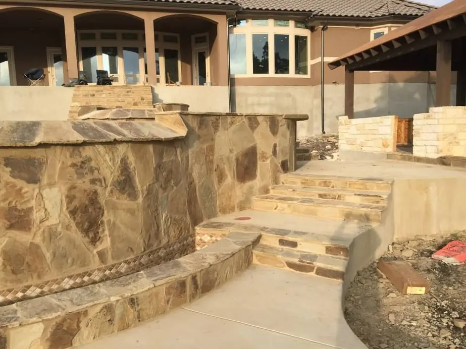 Flagstone-faced raised wall and stone steps being finished beside a stucco patio